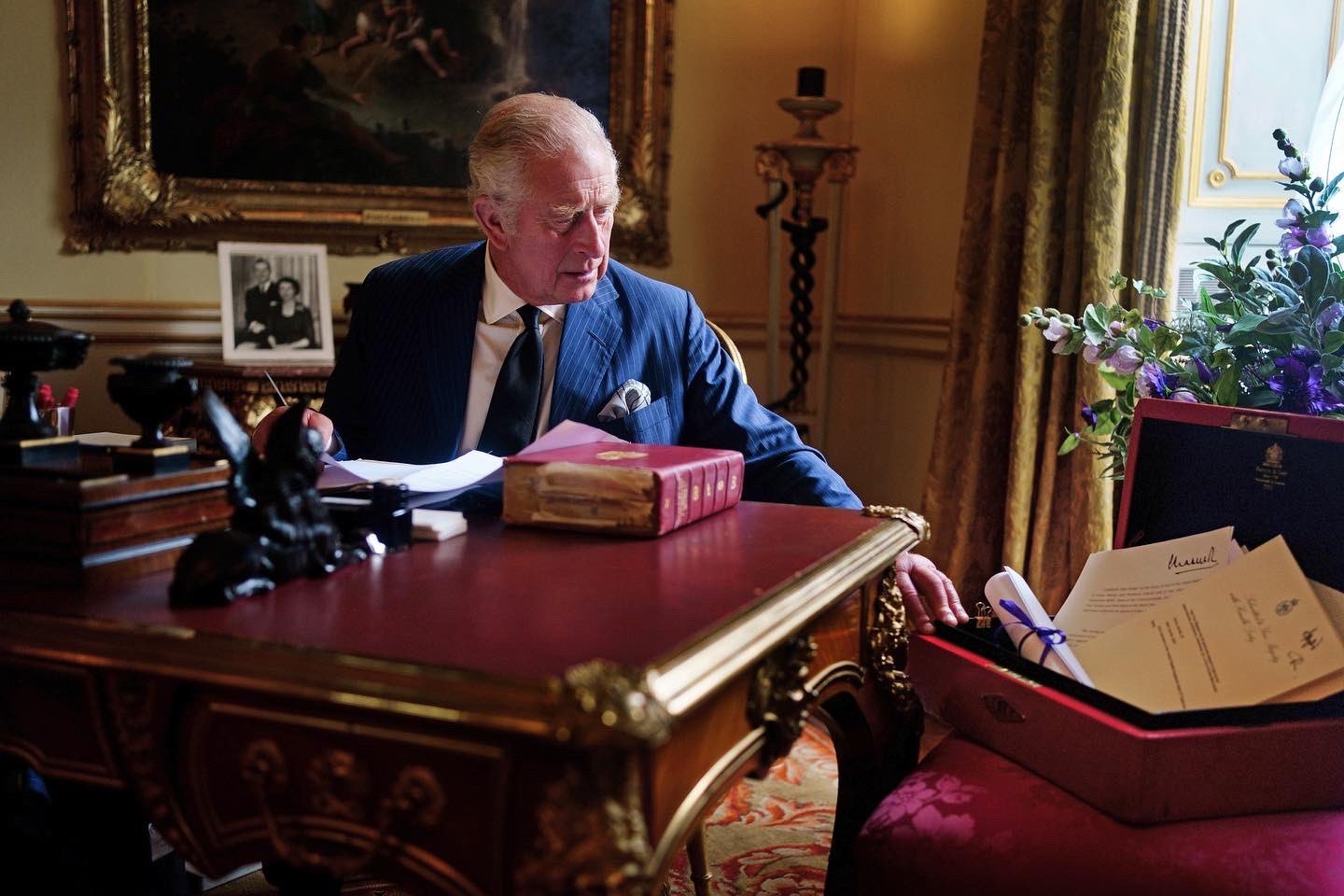 The King sits at his desk with his red box of official government papers.