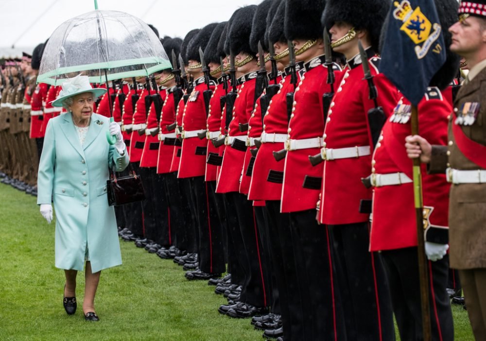 Her Majesty The Queen, Colonel-in-Chief Scots Guards, inspects the 1st Battalion Scots Guards and F Company Scots Guards.

As the heavens opened with soft penetrating rain reminiscent of the Highlands Her Majesty The Queen, Colonel-in-Chief Scots Guards, presented new Colours to the 1st Battalion Scots Guards and F Company Scots Guards in the Gardens of Buckingham Palace. The wisest of the 2,200 assembled guests endured the unrelenting downpour beneath umbrellas, others trusting the fine forecast and unprepared for a turn for the worse, bravely bore the torrent that ensued with typically good British humour. The presentation of new Colours is a rare honour for all soldiers and officers involved and this new set of Colours is the first the company has received since 2002. 
 
On the lawns in front of the Bow Room, Buckingham Palace, The Queen inspected the parade and presented the new Colours to The 1st Battalion and F Company Scots Guards.  While bearskins dripped, and the shoulders of service dress turned a darker shade of khaki, the soldiers stood proud in front of their Colonel in Chief. 

Sgt Rupert Frere RLC / MoD Crown Copyright