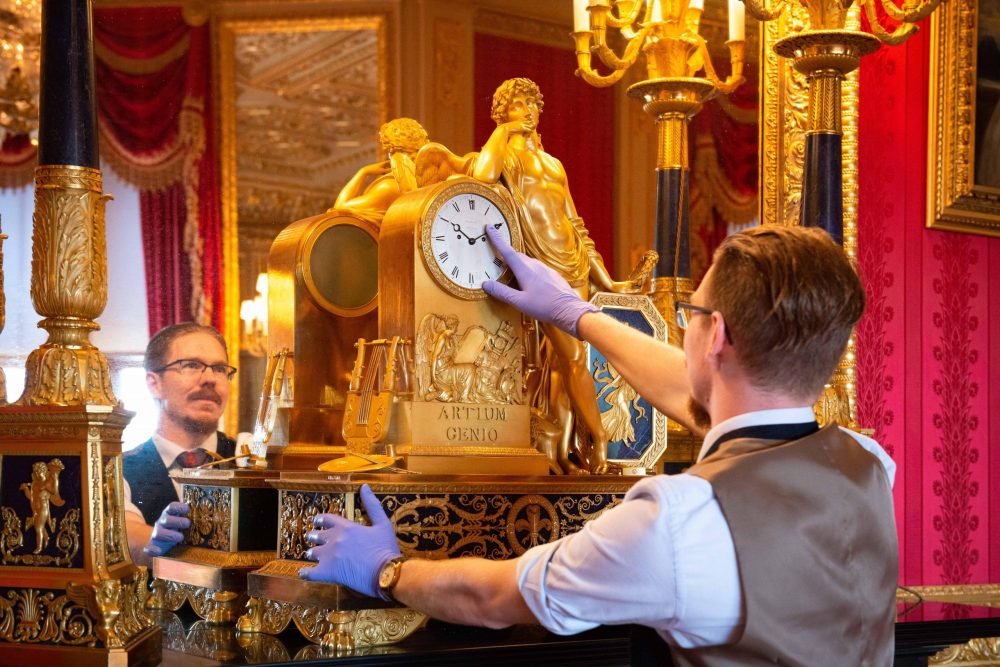 An early 19th-century French mantel clock in the Crimson Drawing Room at Windsor Castle. The winged figure of Apollo leans on the tombstone-shaped clock case, surrounded by the emblems of painting, sculpture and music. The base is inscribed with Artium Genio, ‘The Genius of Arts’. The Crimson Drawing Room is one of the opulent Semi-State Rooms created by George IV, and can be seen on a visit to Windsor Castle during the winter months. (© RCT/Queen Elizabeth II 2020)